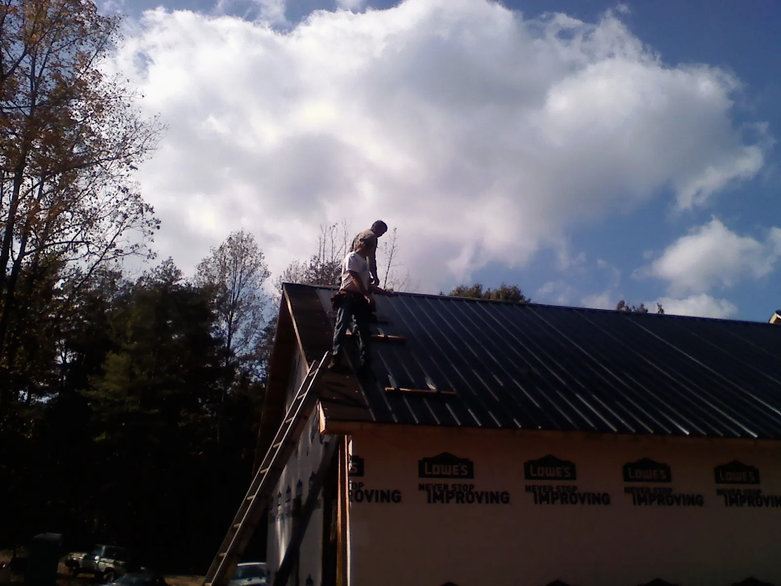 Roofer fastening dark metal panels high against a cloudy sky, from a Roof Inspection job in Lynn